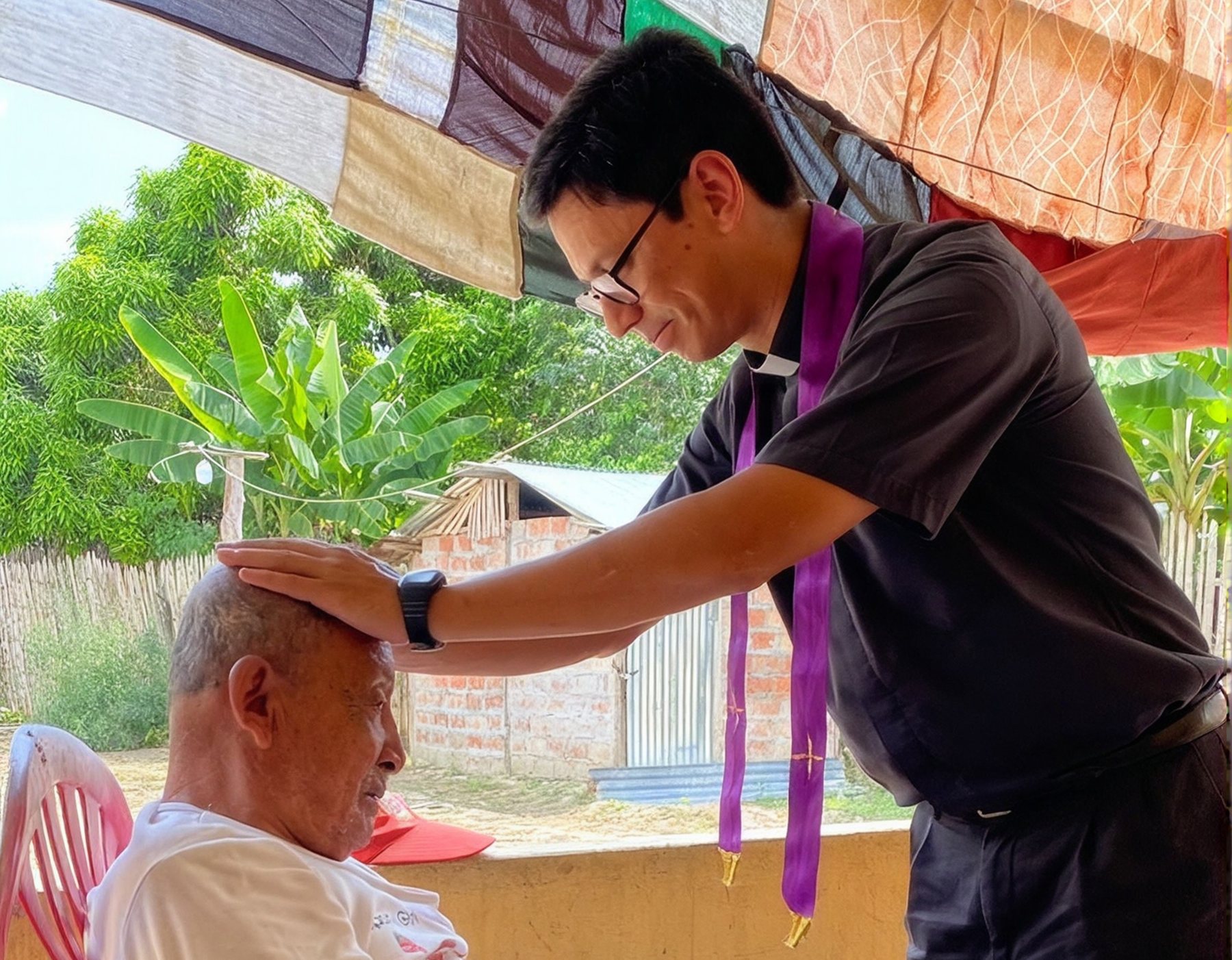 Sacerdote bendiciendo a un adulto mayor durante una visita en la comunidad