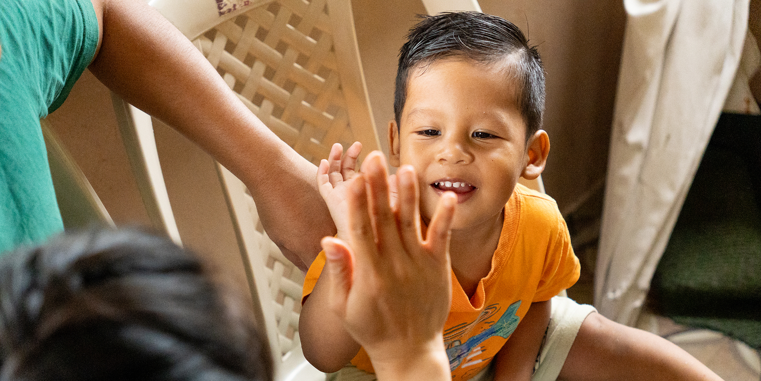 Niño de la comunidad dando un saludo de manos a una voluntaria durante una misión