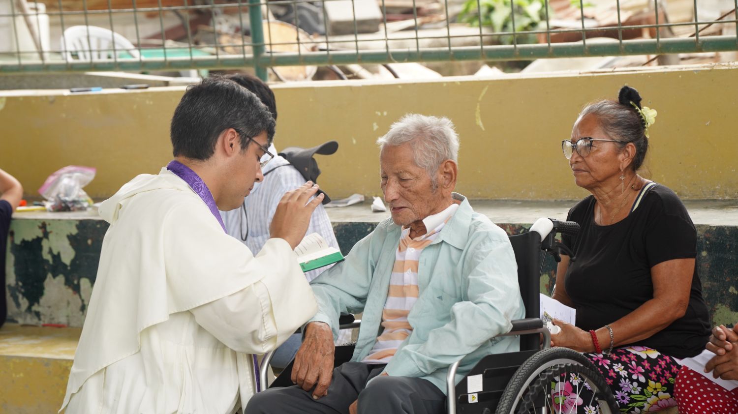 Sacerdote bendiciendo a un adulto mayor en silla de ruedas durante una misión